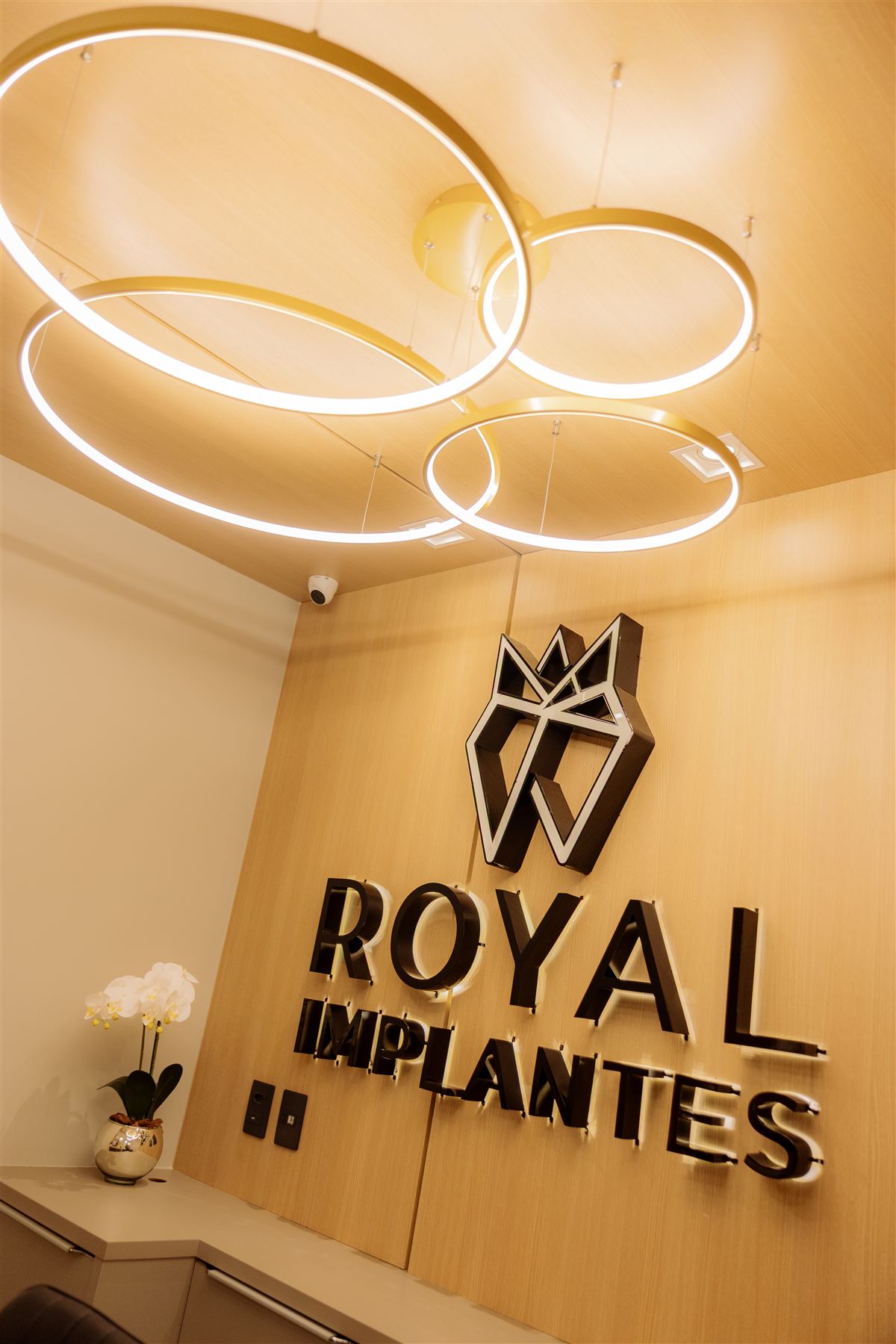 Parede com logo Royal Implantes e luminárias em anéis