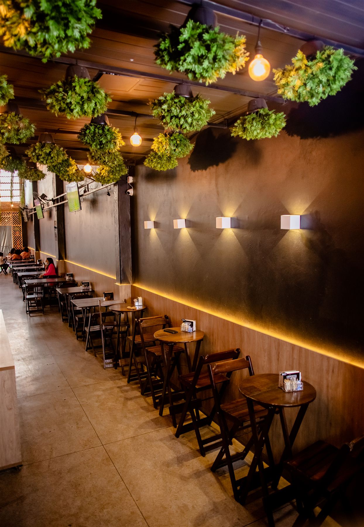 Restaurante Vitrinne com plantas penduradas no teto e iluminação âmbar
