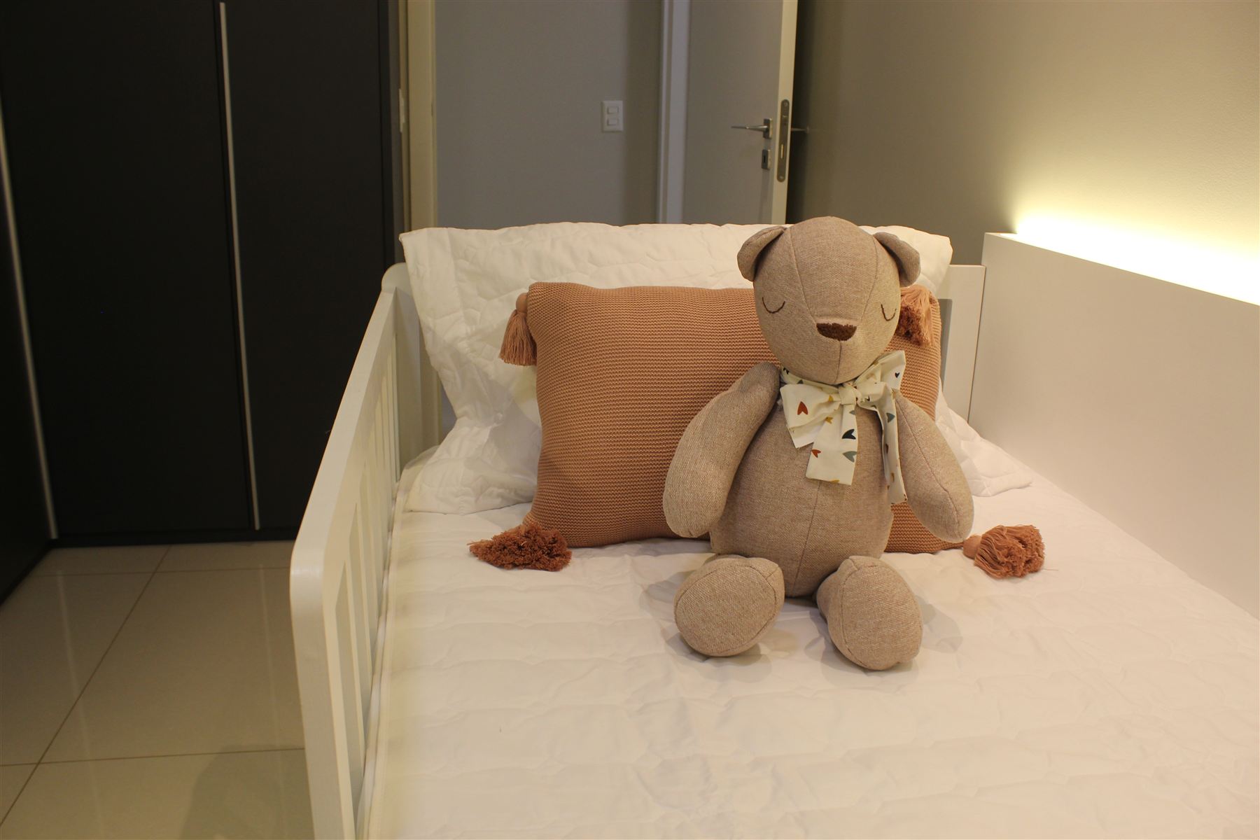 Quarto infantil com cama e ursinho de pelúcia sobre a cabeceira